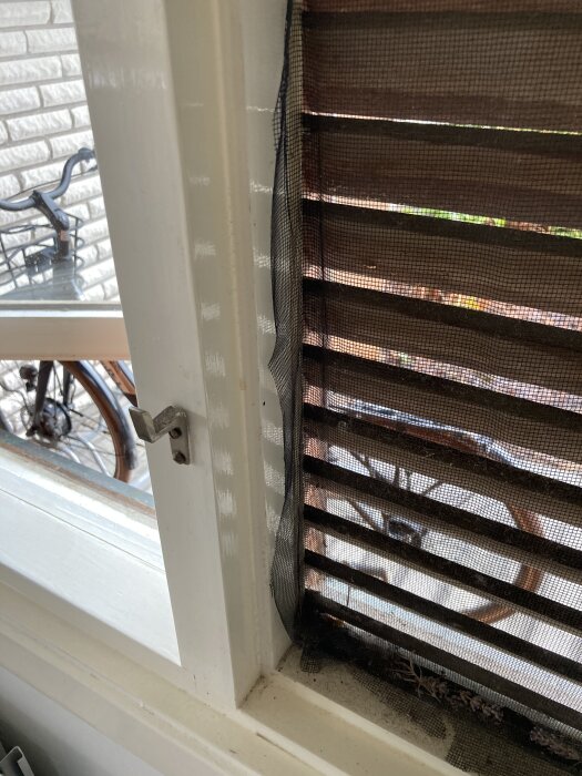 Öppet 60-talsfönster med luftningslucka. Nära syns en cykel utomhus genom persiennerna.