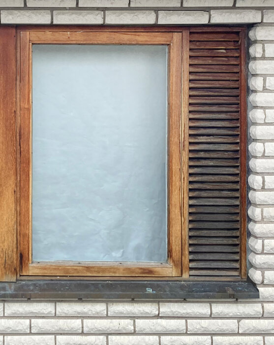 1960-talsfönster med träkarmar och luftningslucka, installerat i en tegelvägg.