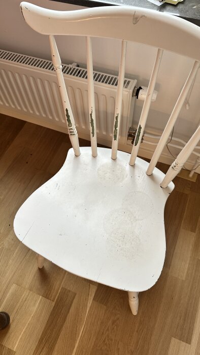 Vit stol med flagnande färg, stående på ett trägolv framför ett element.