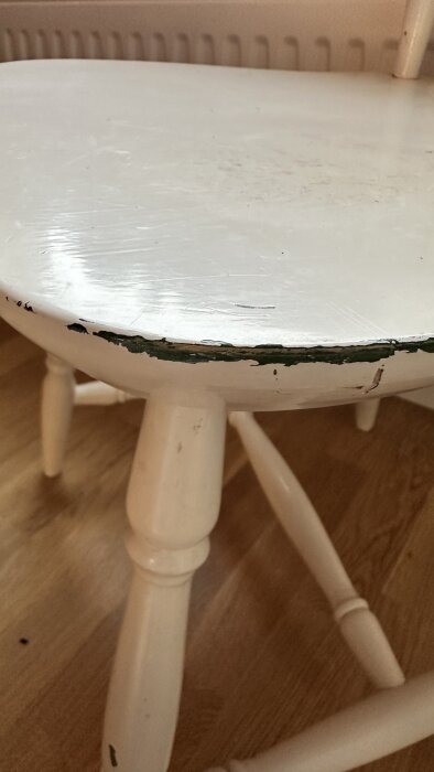 Vit stol med flagnande färg på sitsens kant, stående på ett trägolv.