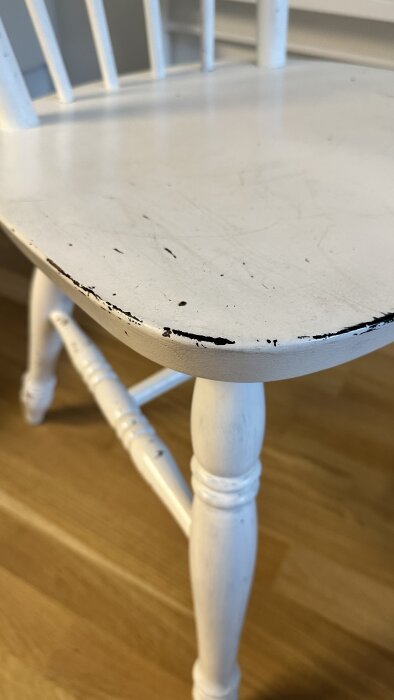 En närbild av en vit stol med slitage och avskavd färg på sitsens kant, på trälaminatgolv.