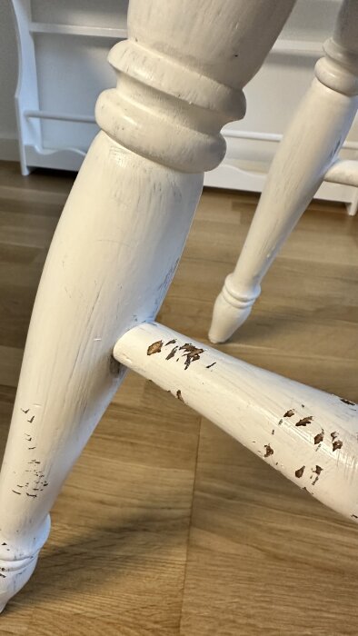 Näskad vit stol med skadad färg på benen, stående på ett trägolv.