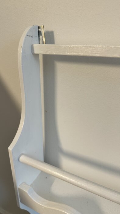 Vit hylla mot en vägg, med två horisontella stänger och monteringsfäste synligt.