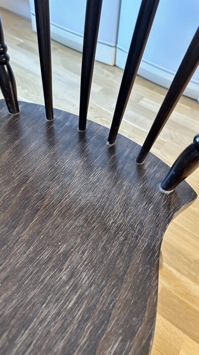 Brun träsits på en stol med svarta stolsben synliga, på ett trägolv.