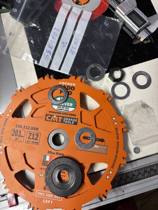 Orange dadoklinga från CMT med distansringar, en förpackning med text och ett skjutmått, placerade på ett arbetsbord.