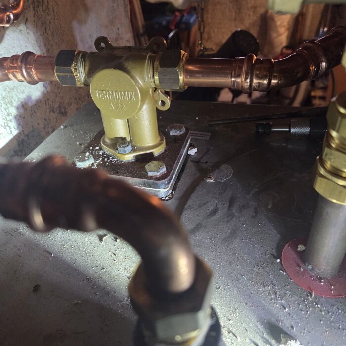 Guldfärgad termomix a22 shuntventil installerad på rörledning i teknisk miljö, omgiven av kopparrör.