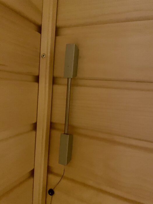 En temperaturgivare monterad ovanför ett bastuaggregat, fastsatt med en tunn tråd mot träpanelen.