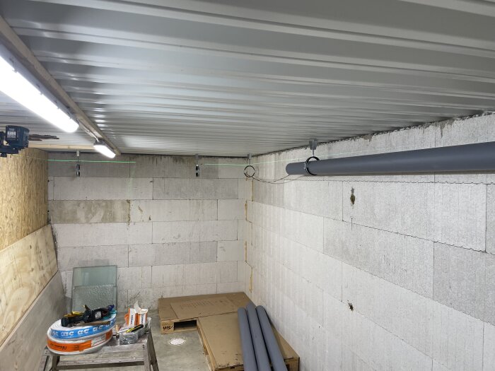 Avloppsrör monterade i taket i ett rum med betongväggar och verktyg på en arbetsbänk.