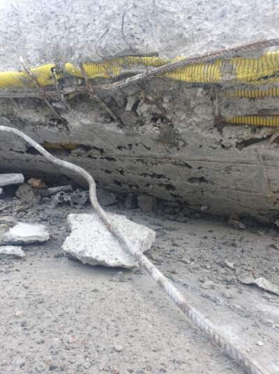 Skadad betongplatta med exponerade rör och armeringsjärn synliga i trasig betong, tecken på felaktig konstruktion och rördragning.