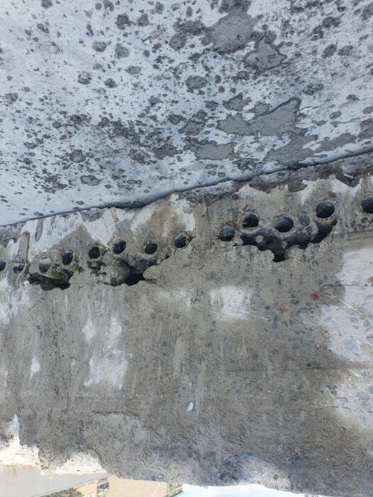 Betongplatta med synliga rör och ojämn yta, där rörledningar passerar genom bottenplattan. Potentiell byggnadsskada på grund av felaktig rördragning.