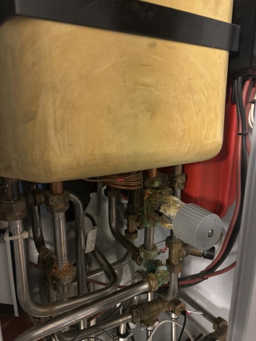 Vattenvärmare med rostiga och korroderade röranslutningar i ett trångt utrymme.