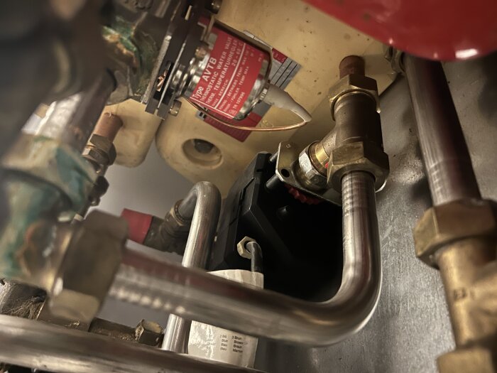 Rör och kopplingar runt en varmvattenberedare, eventuellt med rost, som orsakar värmeproblem i duschvattnet.