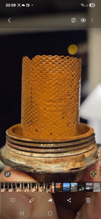 Rostigt filter från fjärrvärmecentral med synliga beläggningar som fastnat i nätstrukturen, hålls i handen för visning.