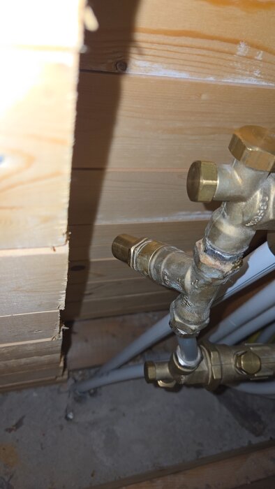 Bypassventil med rörledningar för värmesystem under golvet, omgiven av träpanel, del av frånluftsvärmepumpinstallation.