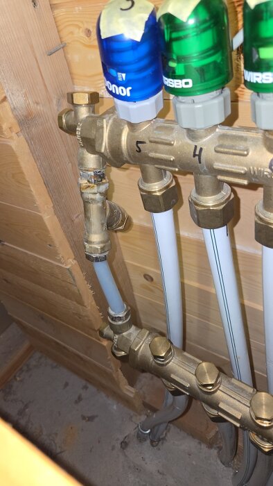 VVS-system av mässing med märken och rör för en frånluftsvärmepump, synlig bypass och ställdon i ett trähus.