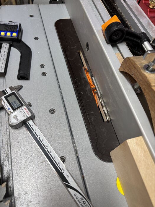 Bordssåg med inställd digital kaliper och träbit, omgiven av verktyg för träbearbetning.
