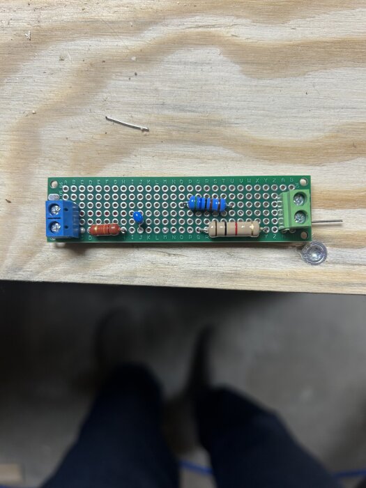 En prydligt monterad elektronikkrets på ett kopplingsdäck med flera motstånd, en diod och skruvplintar, placerat på en trären yta.