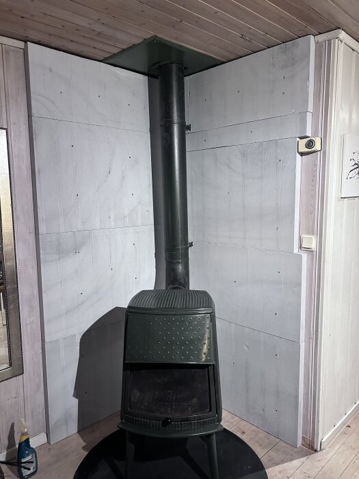 Kamin med kalciumsilikatskivor monterade på väggarna bakom, rökröret nära väggen.