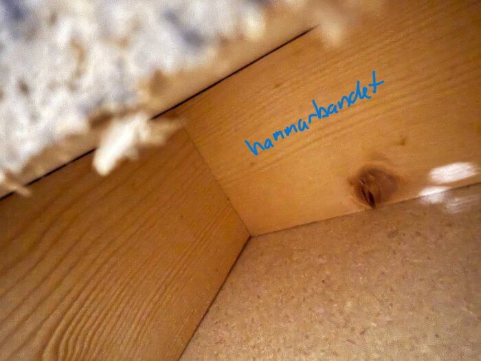 Närbild på en innervägg med träreglar och ett markerat "hammarbandet" med blå text, synlig trästruktur och spånskiva.