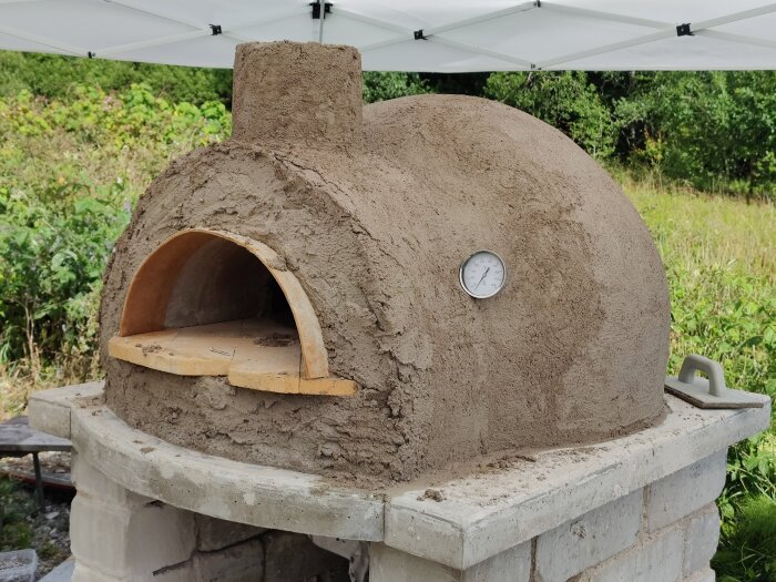 Utomhus vedugn i lera med termometer och tegeltak, byggd på en cementbas.