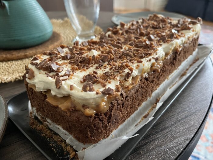Banoffeekladdkaka med krossade mariekex, kolasås, skivade bananer, grädde och hackad dajm på toppen på ett bord.