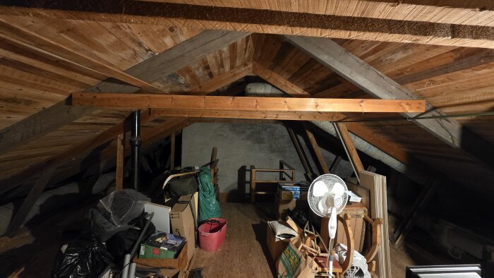 Vind med lågt tak, synliga takstolar och diverse förvarade föremål som kartonger och en fläkt.