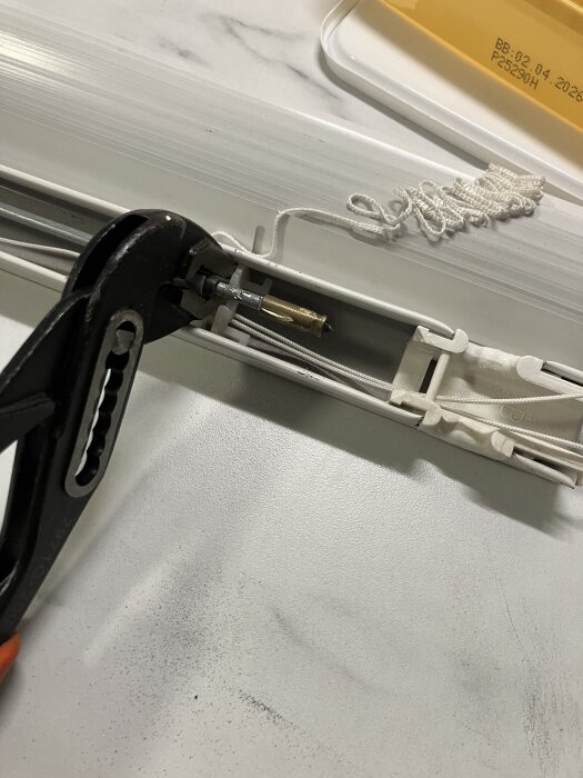 Verktyg håller en horisontell stång i en gardinmekanism; en tång används för att staga upp stången medan den kapas.