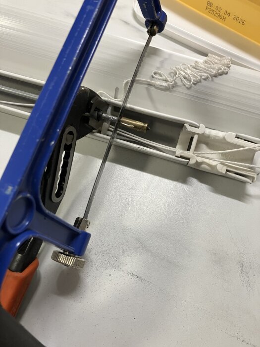 En bågfil skär av en horisontell stång med hjälp av en tång på ett bord.