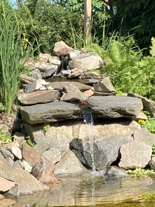 Stenlagd bäck med rinnande vatten och omgivande växtlighet vid trädgårdsdamm.