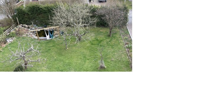 Grönskande trädgård med en liten damm och hängmatta mellan träd. Omgiven av häckar och kullar med stenar vid dammkanten.