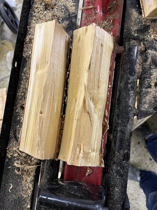 Två kluvna björkvedskärnor på en snickarbänk, med träflisor och sågspån runt dem.