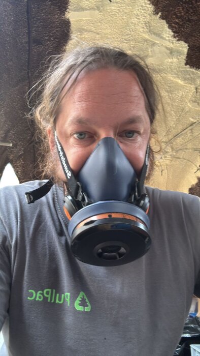 Person bär en skyddsmask under arbete med kork och silikon för att jämna ut väggar i en husvagnsrenovering.