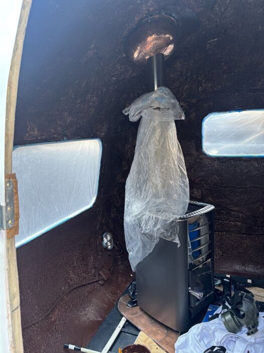 Inre av husvagn med brunsvart korkspackel på väggarna, kaminen skyddad med plast. Utjämnad yta för isolering och jämnare applicering av material.
