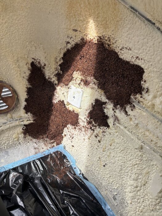 Malda korksmulor ligger utspridda på en ojämn vit vägg av PU-skum i ett rum under renovering. En plastduk skyddar golvet nedanför.