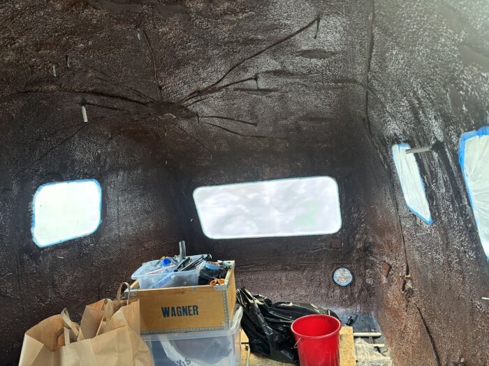 Interiör av husvagn med korkbeklädda väggar, arbete med utjämning pågår, utrustning och verktyg i förgrunden, fönster täckta.