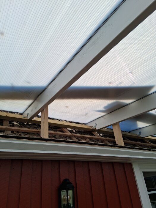 Trasigt tak med byggställning och genomskinligt takskydd, ovanpå ett rött hus.