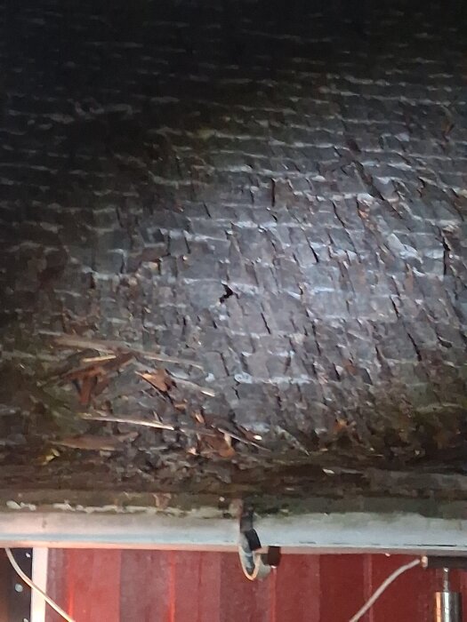 Sprucket och skadat tak med lösa bitar och sprickor, fotograferat i något mörker med belysning på det skadade området.