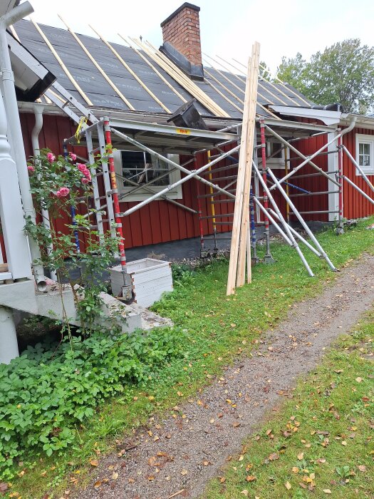 Rött hus med pågående takrenovering, byggställningar, lösa brädor mot väggen och blottat tak med undertak synligt.