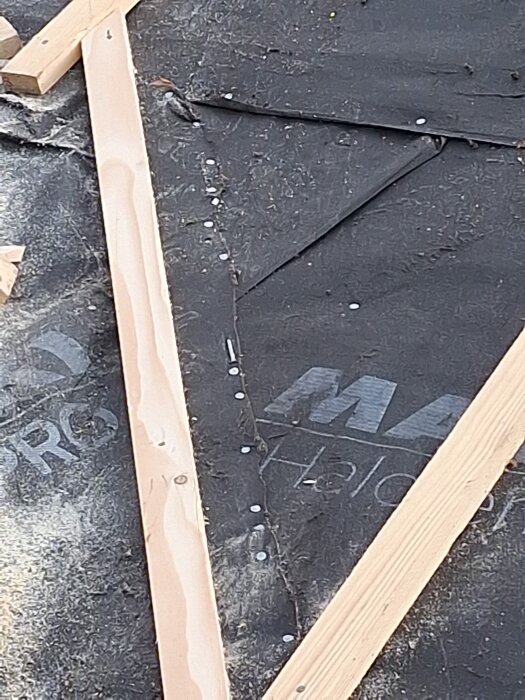 Träreglar ovanpå svart takmaterial med synliga spikar, troligen under arbete för nytt tak.