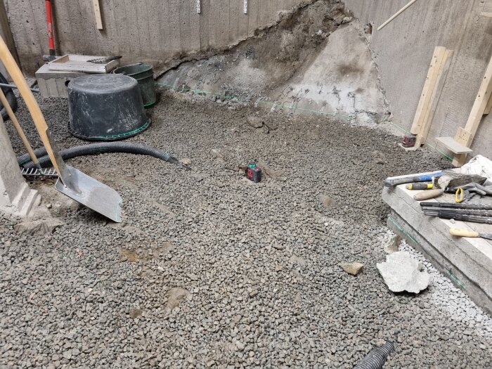Gruslagd yta med verktyg och hinkar vid en betongvägg, där sprickor i berget syns. En laser och olika verktyg är utspridda.