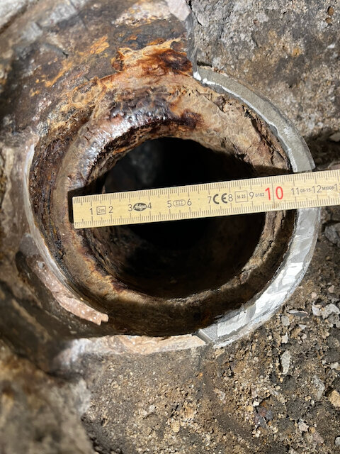 Gammalt kapat rör med måttstock som visar innerdiameter cirka 90-95 mm, omgiven av jord och stenar.