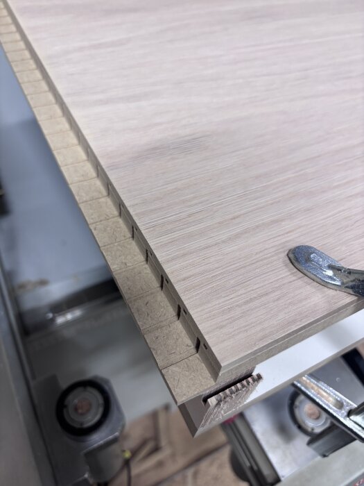 Närbild av träplanka med falsad kantlist under limning i en verkstadsmiljö, verktyg synliga i bakgrunden.