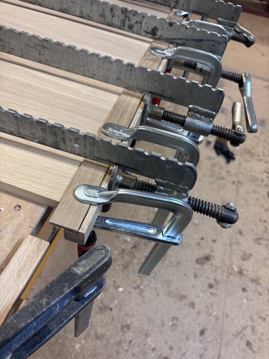 Limning av svängda träluckor med C-klämmor på arbetsbänk i verkstad.