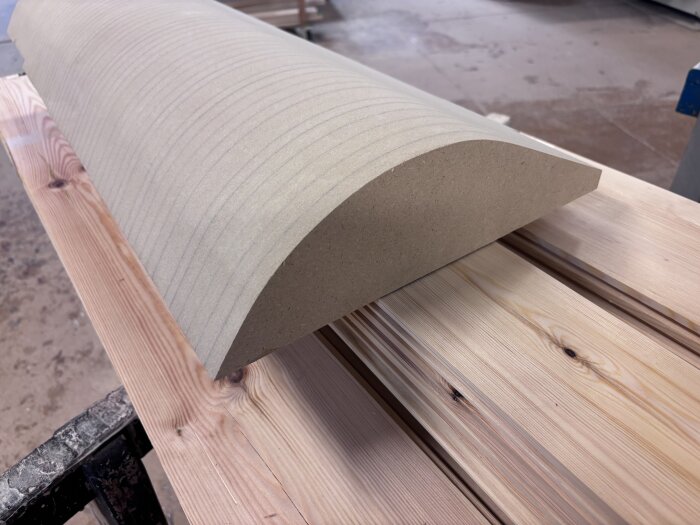 Svängd MDF-skiva på träbänk, förberedelse för limning av kantlist, del av byggprojekt med skåpsluckor och lådfronter.