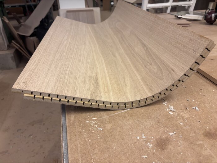 Böjd träskiva med fasade kantlister för ett hörnskåp på en arbetsbänk i en verkstad.