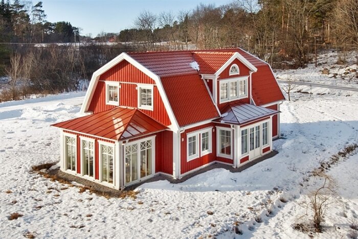 Rött hus med vitmålade detaljer och ett rött, brutet tak. En sidobyggnad i glas är ansluten till kortsidan. Snölandskap.