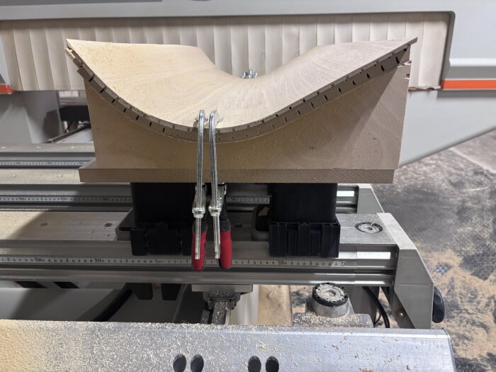 Svängd träbit i verkstad, fastklämd för bearbetning av böjd kantlist på arbetsbänk.