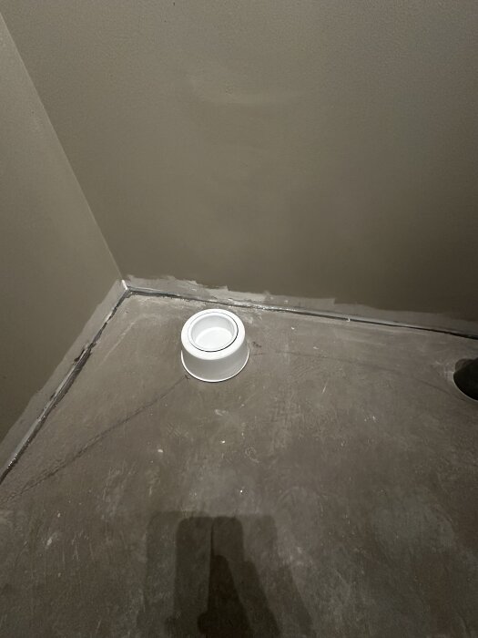 Flytspacklat golv i ett badrumsprojekt där ett vit rund markeringsring ligger nära ett hörn med ojämn yta vid väggen, potentiellt fall i golvplan.
