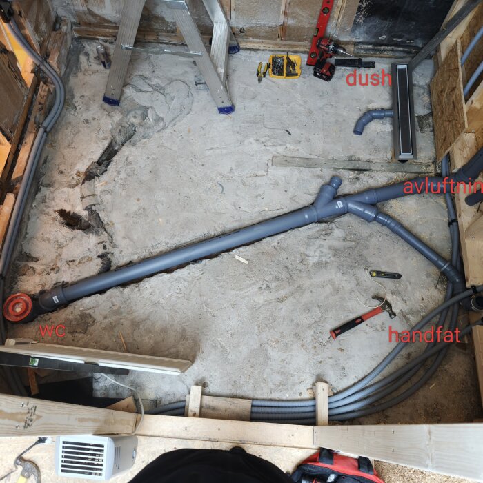 Rörinstallation i badrum under renovering. PVC-rör leder från dusch till WC, handfat och avluftning. Verktyg och material synliga på golvet.