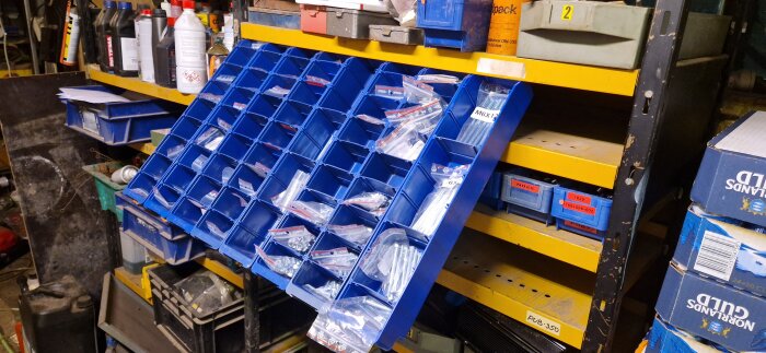 Blå verktygslåda fylld med sortimentpåsar av skruvar på en hylla i ett verkstadsutrymme.